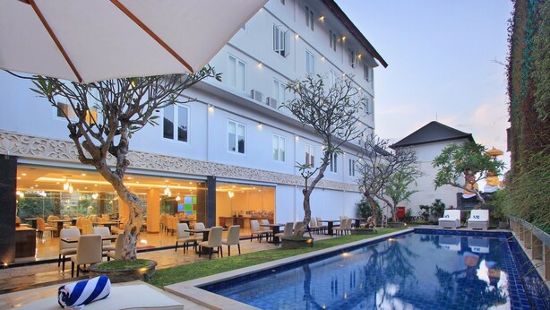 Un patio de hotel con piscina, mobiliario exterior y un restaurante.