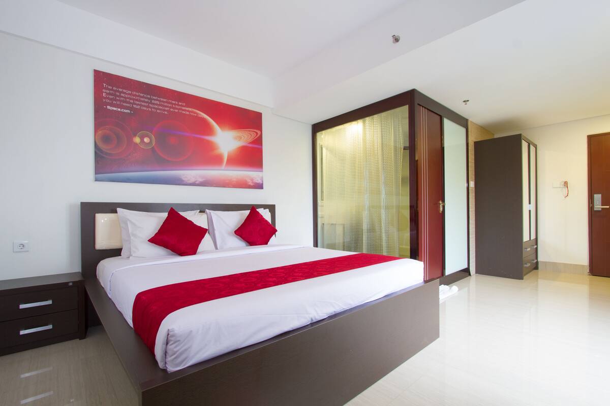 Una habitación de hotel moderna con una cama grande, una mesita de noche, una pared de acento roja y un ventanal con persianas.