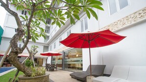 Un patio con un edificio blanco, mobiliario exterior y una piscina.