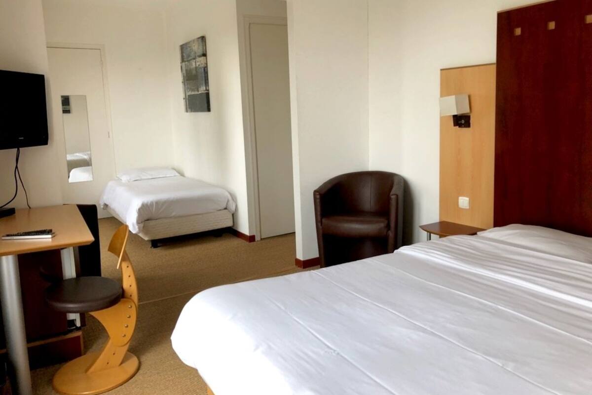 A hotel room with a large bed, a desk with a chair, a smaller bed, a chair, and a TV.