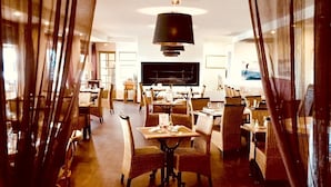 A dining area with a central table, surrounded by wicker chairs, and a modern chandelier. - Hôtel La Chaloupe (Port-des-Barques)