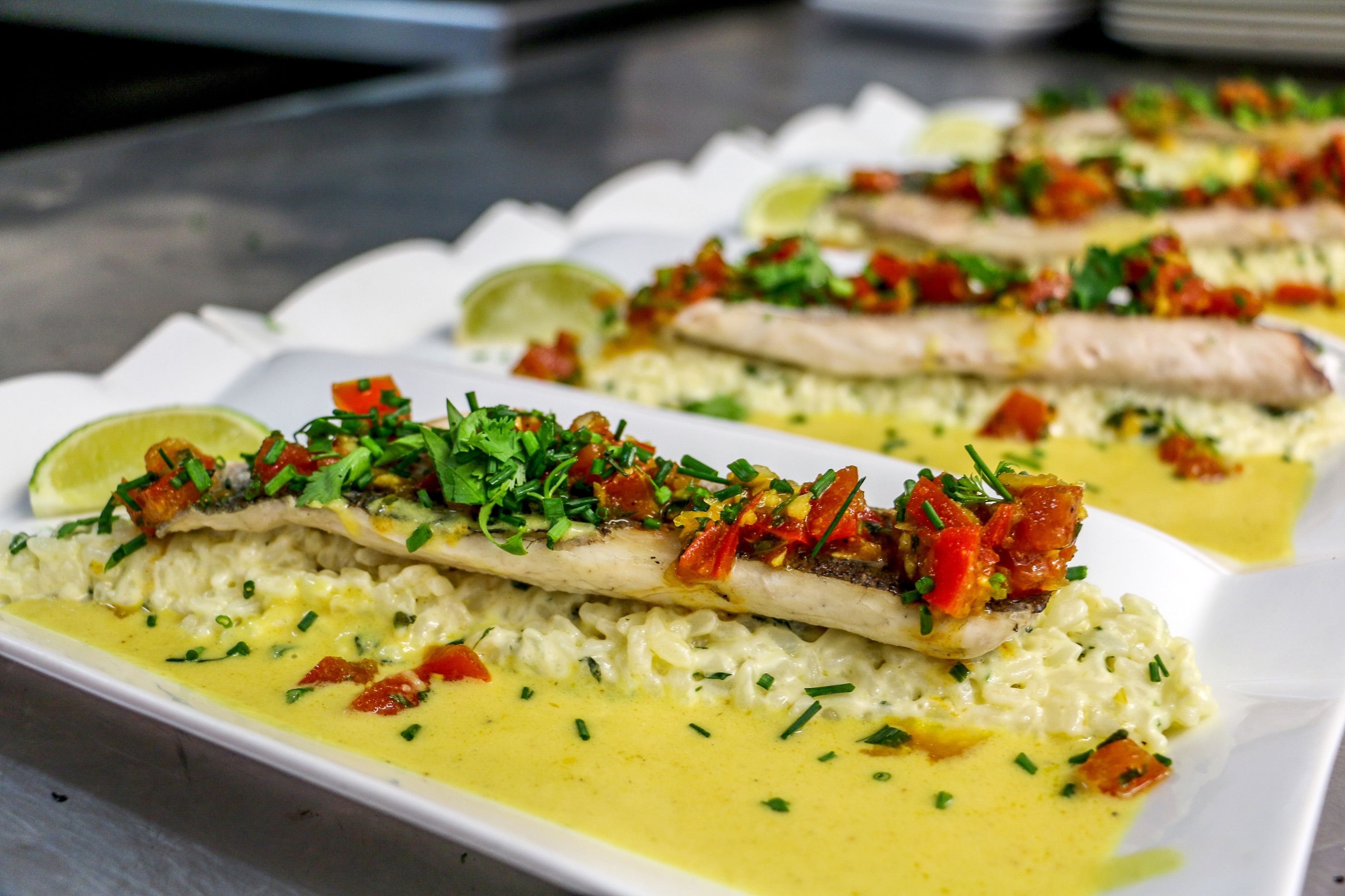 A dish with fish, rice, and a yellow sauce, garnished with herbs and diced tomatoes.