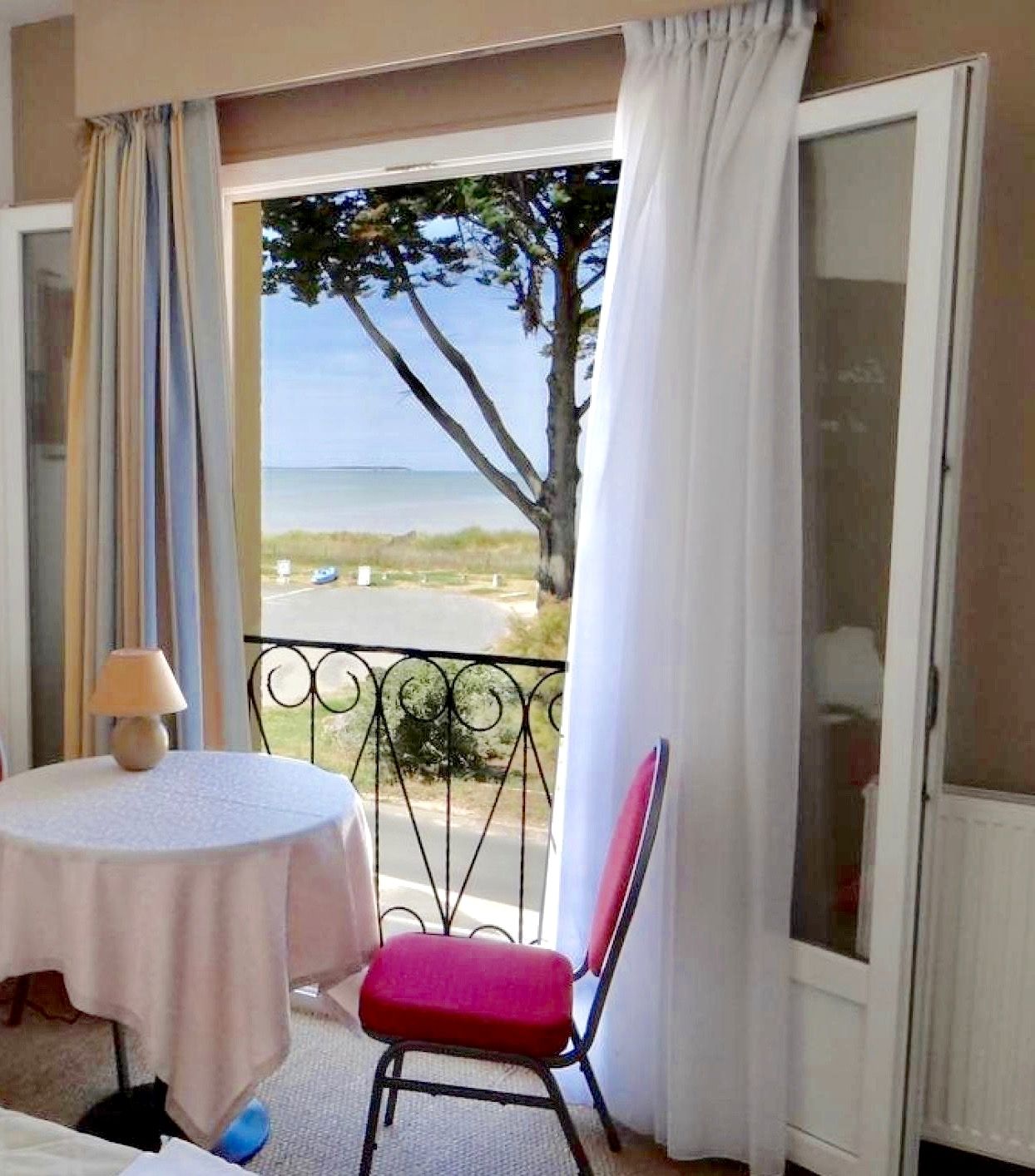 A room with a balcony, a table with a lamp, and a chair.
