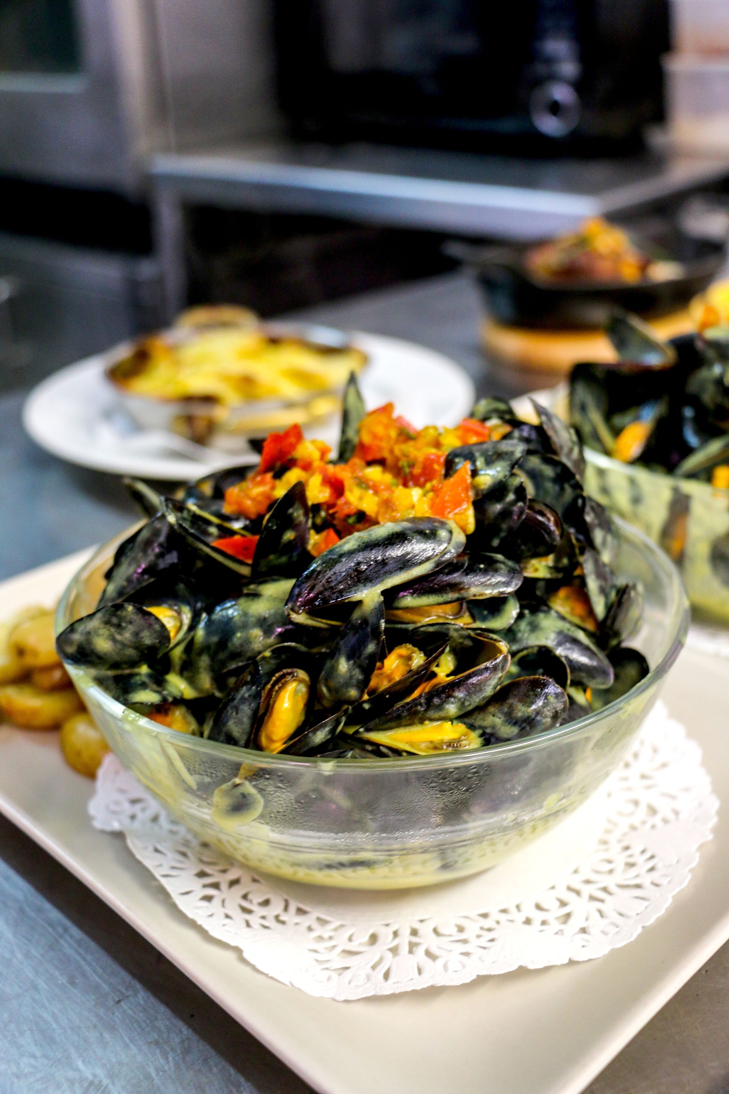 A clear glass bowl of mussels on a white doily.
