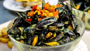 A clear glass bowl of mussels on a white doily.
