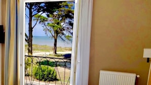 A bedroom with a bed, a view of the beach, and a balcony with a railing. - Hôtel La Chaloupe (Port-des-Barques)