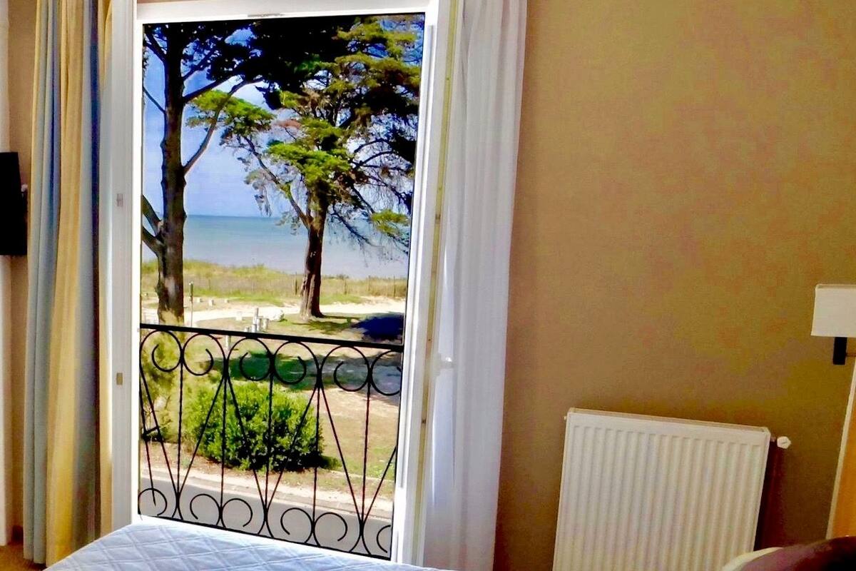 A bedroom with a bed, a view of the beach, and a balcony with a railing.
