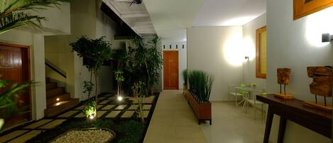 Un interior moderno con suelo a cuadros, una escalera, plantas en macetas y una pequeña mesa con sillas.
