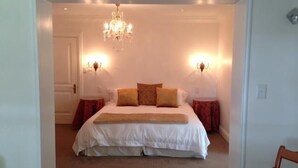 A bedroom with a large bed, two bedside tables, a chandelier, and wall sconces.