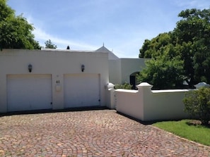 Un edificio con dos puertas de garaje blancas, un camino de adoquines y una pared blanca con un pequeño ventanal.