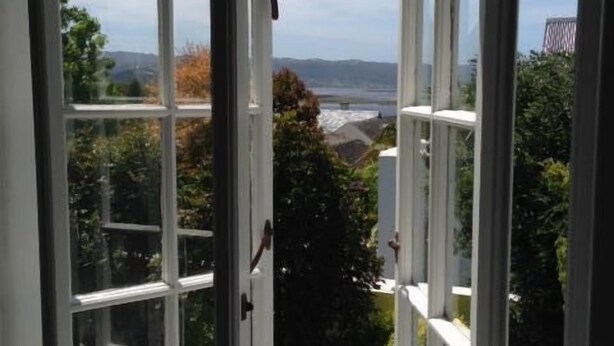A view through a large window with multiple panes, revealing a landscape with greenery and distant hills.
