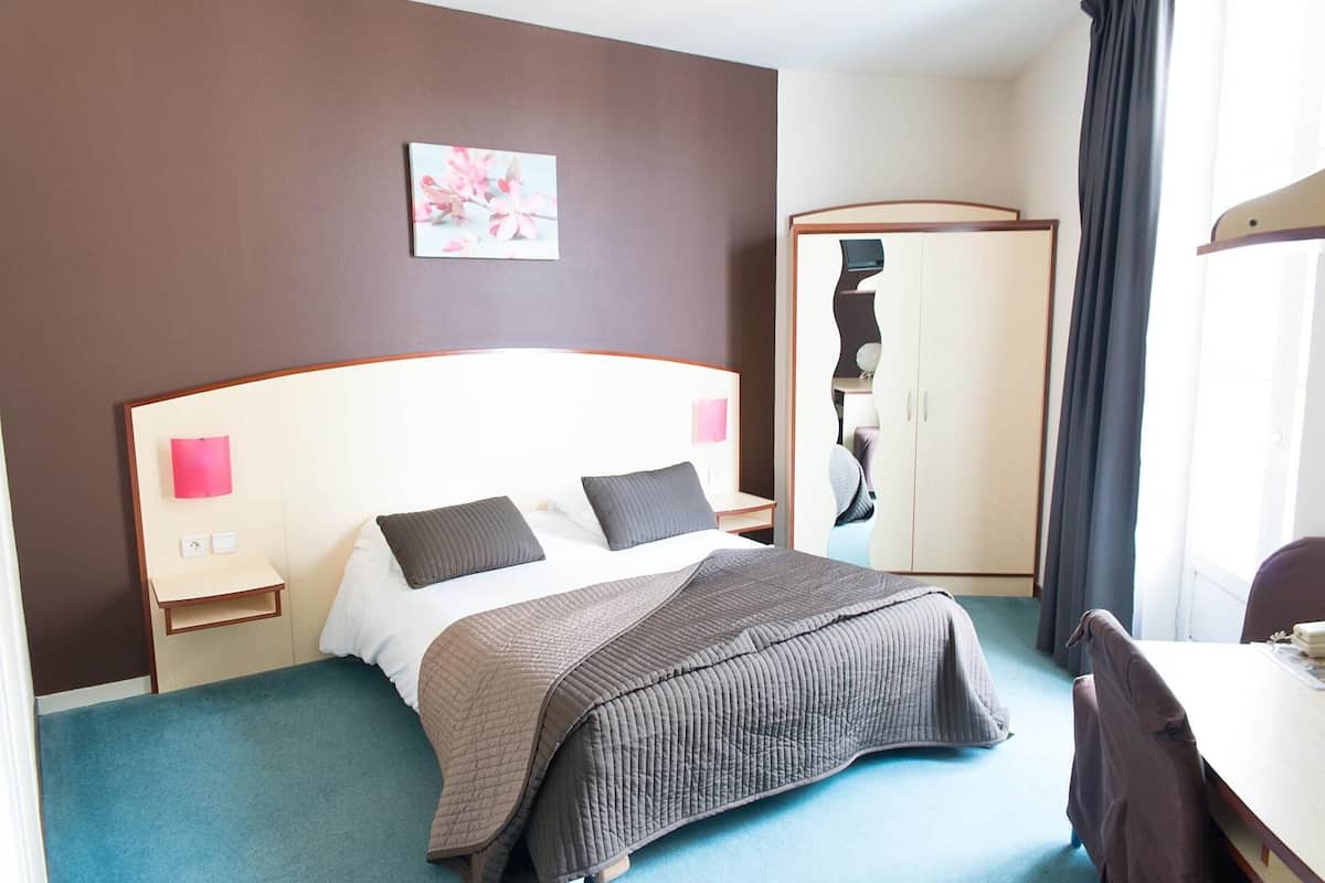 Une chambre d’hôtel comprenant un lit, des tables de chevet, une armoire et un bureau.