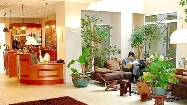 A hotel lobby with a reception desk, seating area, and potted plants. - Hôtel de France (Montmorillon)