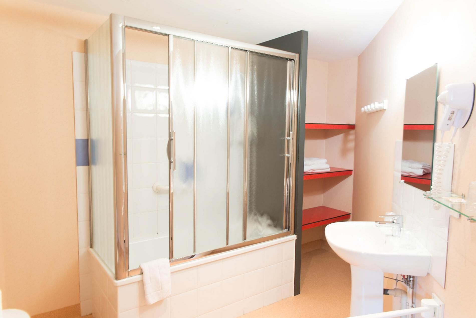 Une salle de bain avec une douche à parois de verre, un lavabo blanc et une étagère rouge.