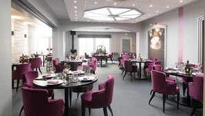 A spacious dining area with round tables and purple chairs, featuring a modern ceiling design and large windows. - Hôtel de France (Montmorillon)