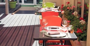 A dining area with tables and chairs, a potted plant, and a wooden deck. - Hôtel de France (Montmorillon)