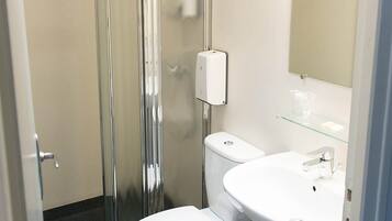 Un baño con cabina de ducha de vidrio, inodoro blanco y lavamanos con espejo.