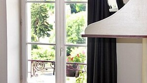A room with a large window, a white lamp, and a view of greenery outside. - Hôtel de France (Montmorillon)