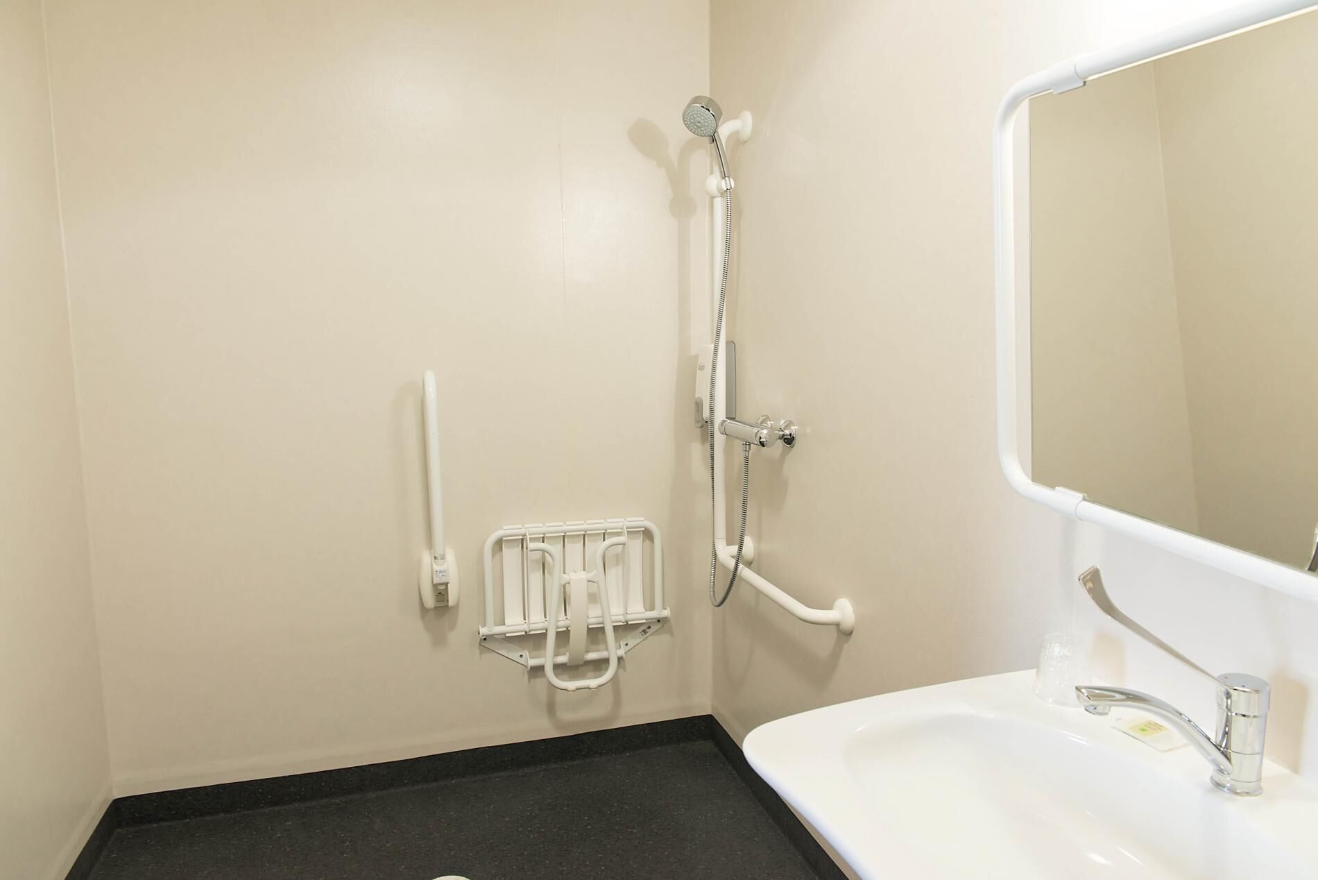 A bathroom with a white sink, a mirror, a shower with a handheld showerhead, and a grab bar.