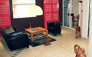 A living room with a sofa, a coffee table, a lamp, and a small table with items on it. There is a red curtain and a door with a glass panel. - Hôtel de France (Montmorillon)