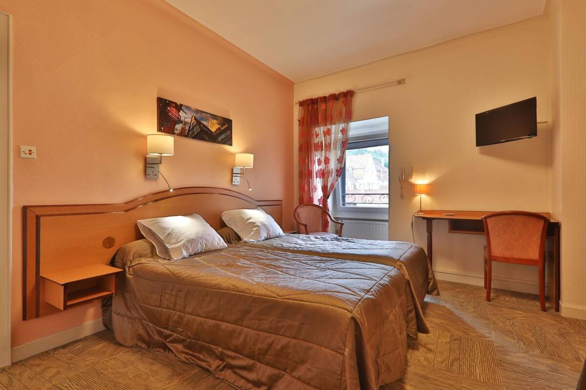 A hotel room with two beds, a desk, a chair, a TV, and a window with curtains.