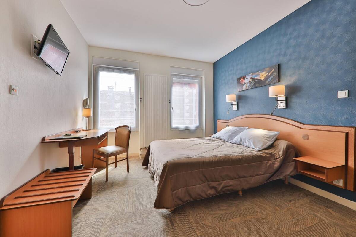 A hotel room with a bed, desk, chair, and a TV mounted on the wall.