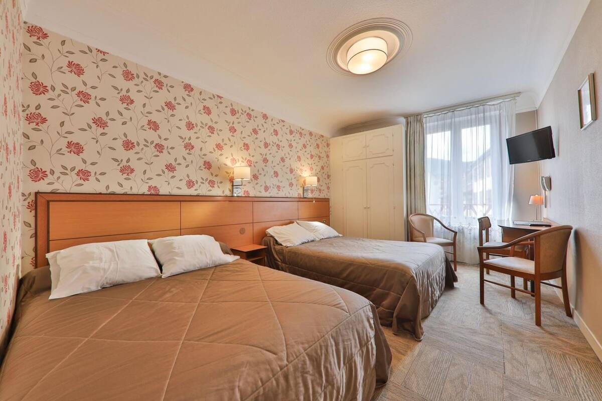 A hotel room with two beds, a desk, a chair, a TV, and a wardrobe.