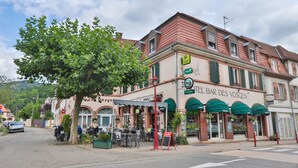 A restaurant with outdoor seating, a sign reading "TEL BAR DES VOSCES," and a view of the street. - HOTEL Bar des VOSGES (Munster)