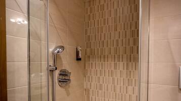 A glass-enclosed shower with a control panel, beige tiled walls, and a white bathtub.