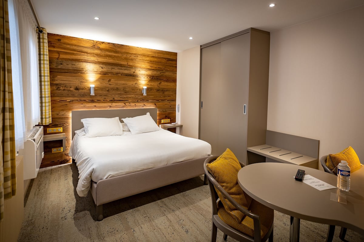 Une chambre d’hôtel comprenant un lit, des tables de chevet, un bureau avec une chaise, un miroir et une armoire.