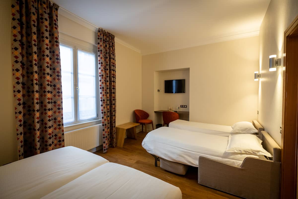 Une chambre d’hôtel avec deux lits, un bureau, une chaise, une télévision et une fenêtre avec des rideaux.