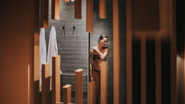 Eine Person in der Dusche, mit einer Ziegelwand und Holzelementen.