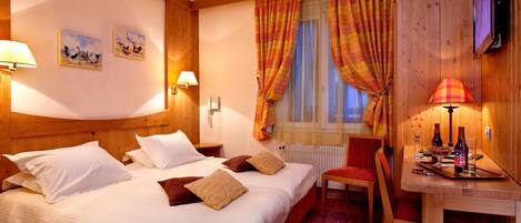 A hotel room with a large bed, two wall-mounted lamps, a wooden desk with a chair, and a television.