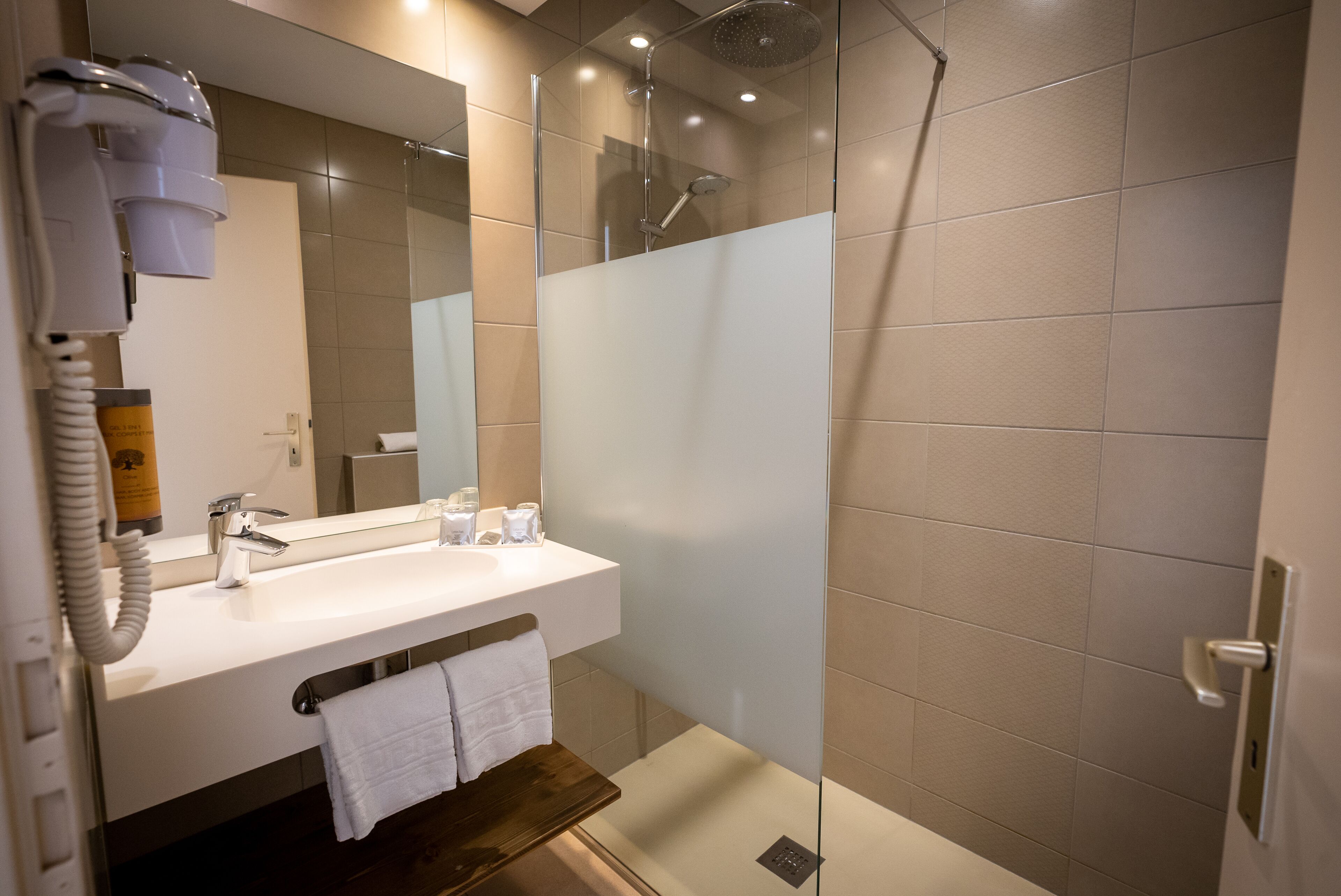 Een moderne badkamer met een douchecabine van glas, een witte wastafel en een haardroger bevestigd aan de muur.