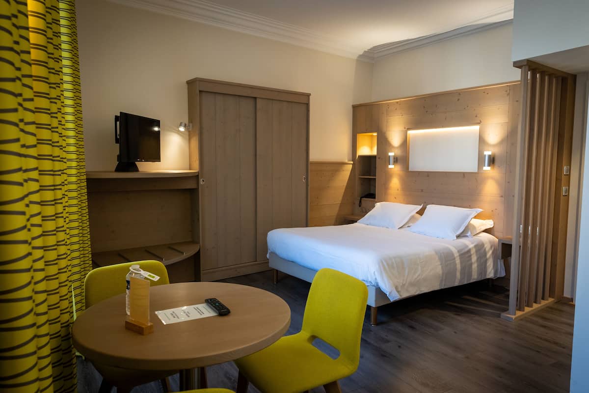 Une chambre d’hôtel comprenant un lit, une table avec une chaise, une télévision et une armoire.