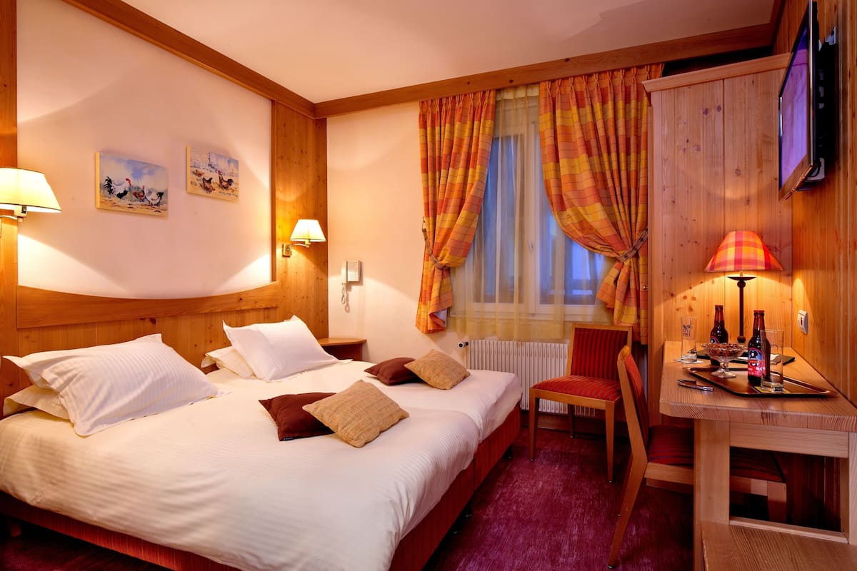 Une chambre d’hôtel comprenant un lit, un bureau avec une chaise, une télévision et des œuvres d’art accrochées aux murs.
