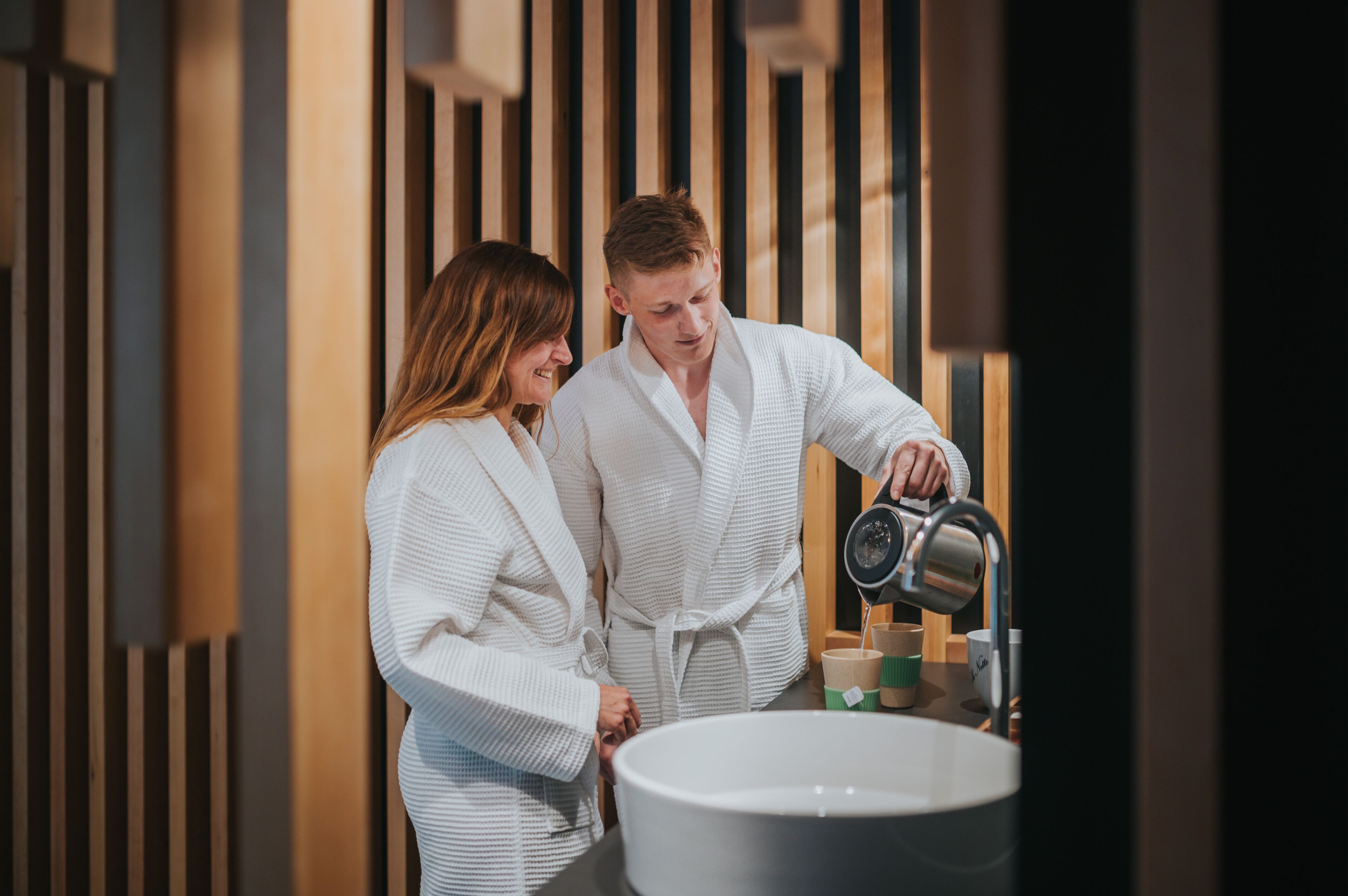 Un couple dans une salle de bain moderne, avec un grand lavabo et un lambris en bois.
