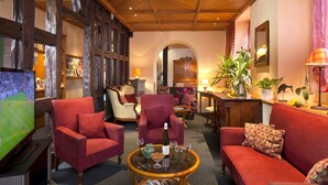 Ein gemütlicher Lounge-Bereich mit rot gepolsterten Möbeln, Holzboden und einem Fernseher, der ein Sportspiel zeigt.