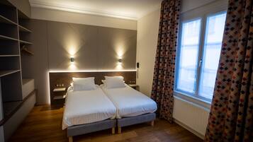 Une chambre moderne avec deux lits, des étagères intégrées, des lampes de chevet et une fenêtre agrémentée de rideaux à motifs.