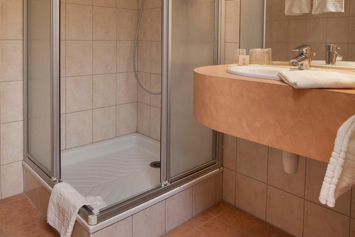 Une salle de bain moderne avec une douche à parois de verre, un meuble-lavabo incurvé doté d’un miroir et un sol carrelé.