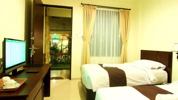 A hotel room with two beds, a desk with a computer and a tray of cups, and a view of a garden through a window.