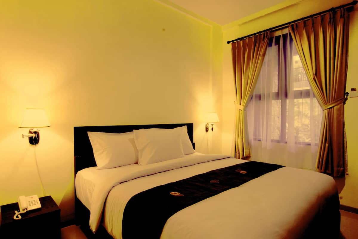 A hotel room with a bed, bedside lamps, a telephone, and curtains.