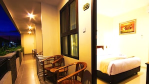A hotel room with a bed, a desk, and chairs. There is a window and a door. - Manggar Indonesia Hotel & Residence (Kuta)