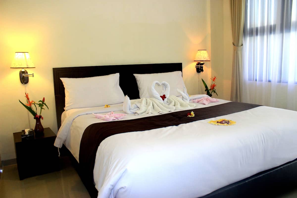 A neatly made bed with white linens, two wall-mounted lamps, and a vase with flowers on a nightstand.
