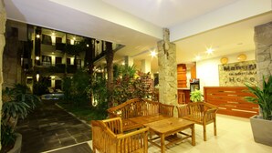 A lobby with a wooden reception desk, a seating area with wooden chairs, a stone pillar, and a staircase leading to an upper floor. - Manggar Indonesia Hotel & Residence (Kuta)