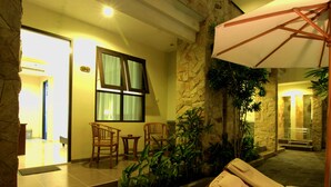 A well-lit indoor area with a stone wall, a wooden bench, and a window with curtains. - Manggar Indonesia Hotel & Residence (Kuta)