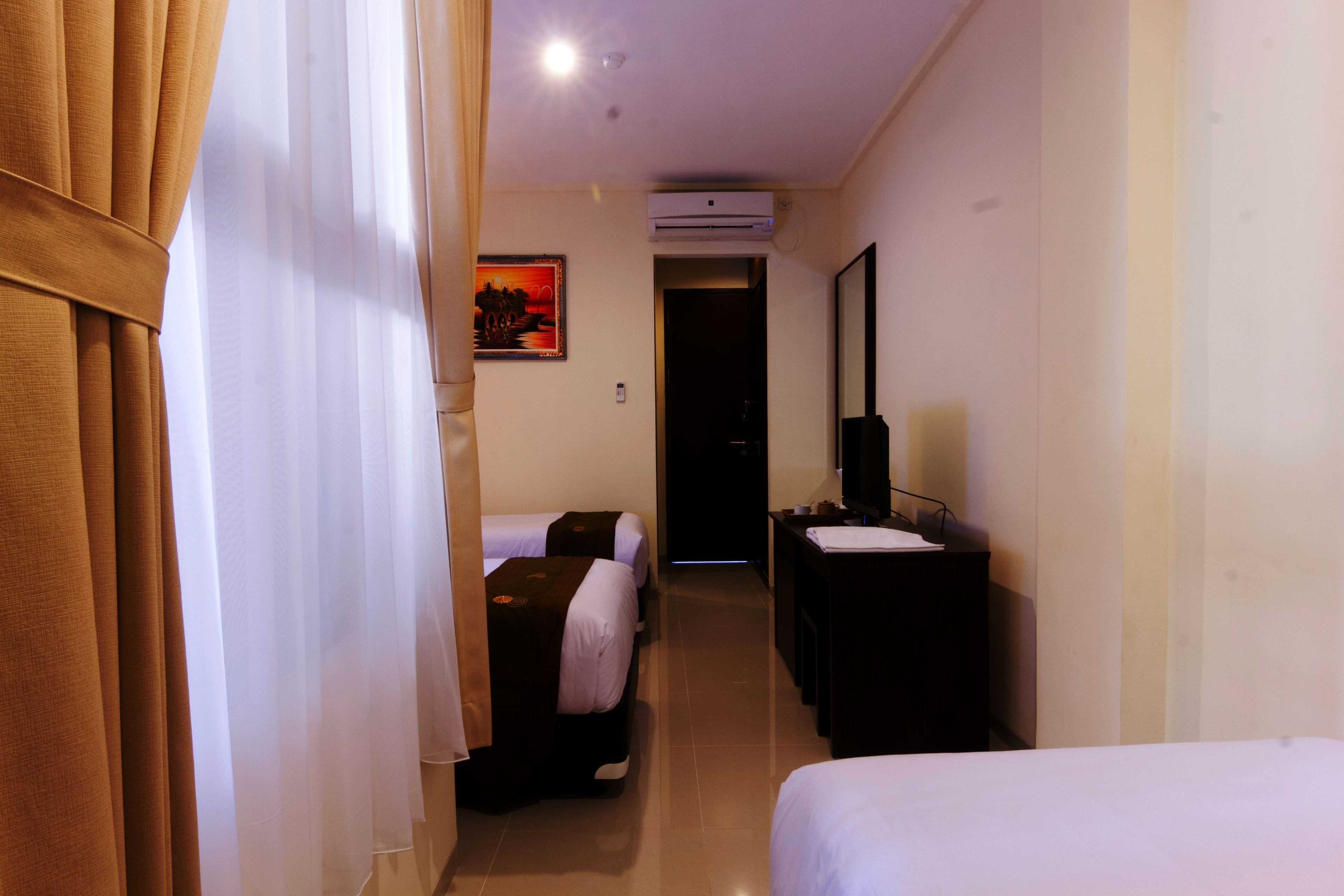 A hotel room with two beds, a desk, a mirror, and an air conditioning unit on the wall.