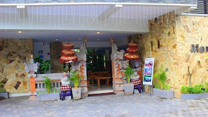 A hotel entrance with a stone facade, a wooden reception desk, and red decorative lanterns. - Manggar Indonesia Hotel & Residence (Kuta)