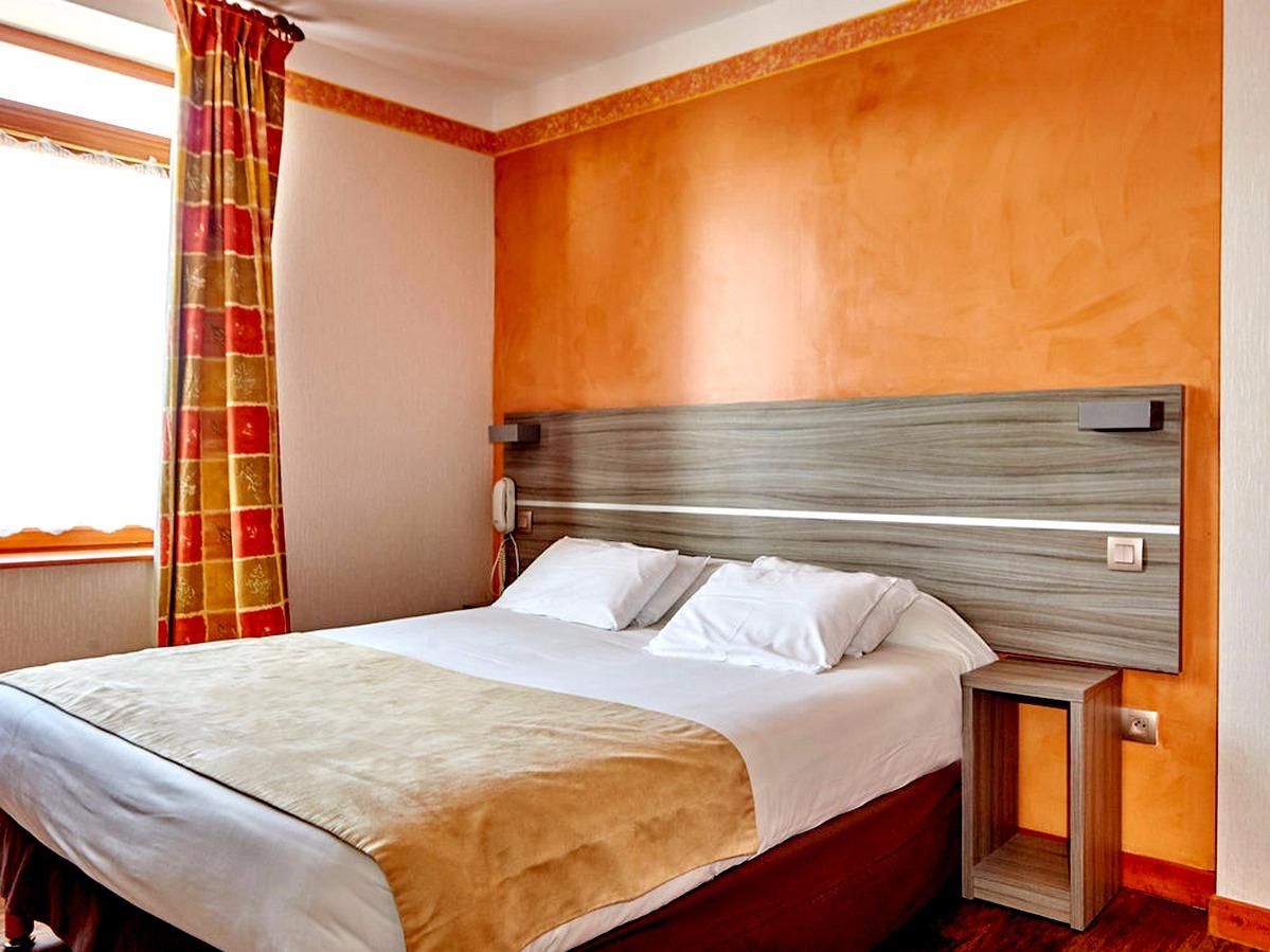 Une chambre d’hôtel avec un grand lit, une tête de lit en bois, une table de chevet et une fenêtre avec des rideaux.