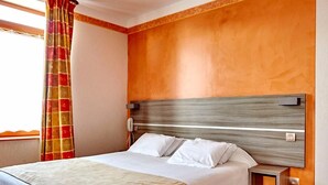 Habitación de hotel con una cama grande, cabecera de madera, mesita de noche y ventana con cortinas.